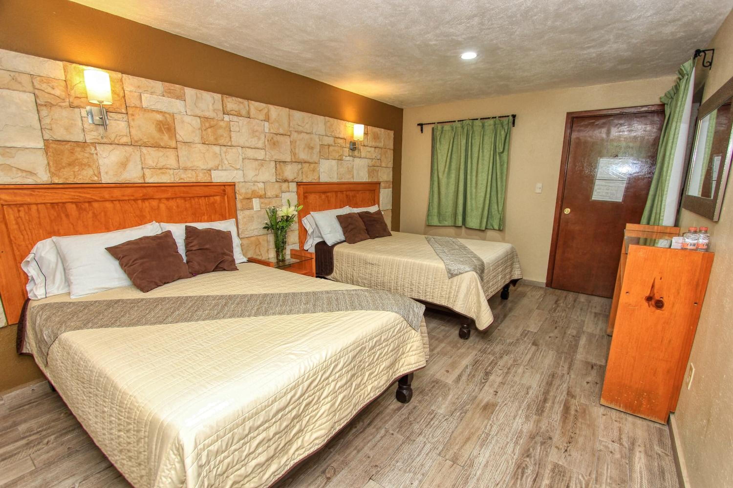 Una habitación de hotel con dos camas, una pared de piedra, una puerta de madera y una cortina verde.