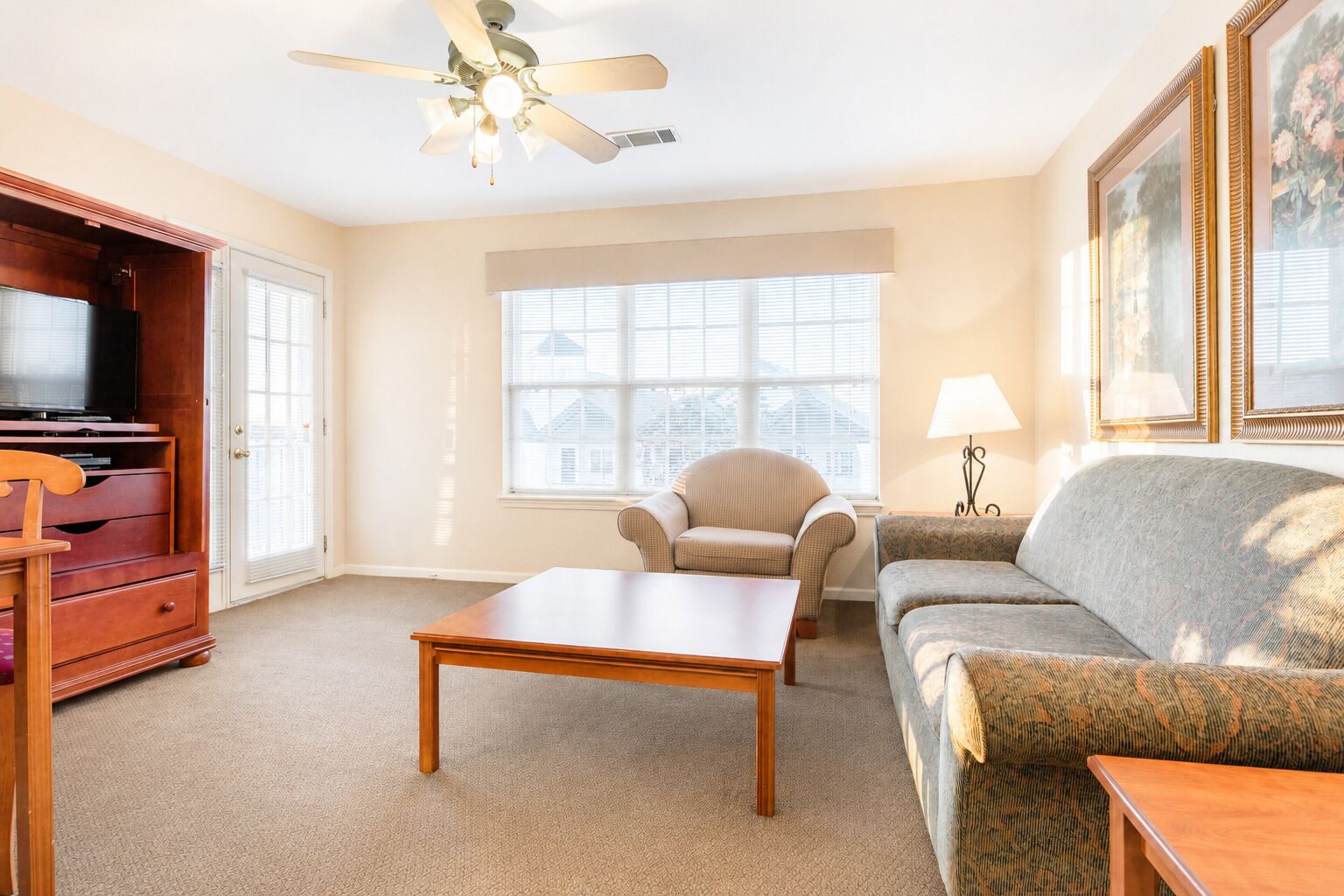 A living room with a wooden TV stand, a ceiling fan, a sofa, a chair, and a table.