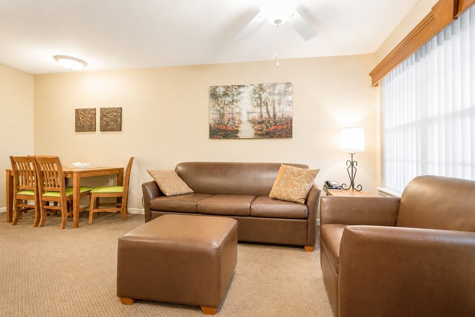 A living room with a brown leather sofa, matching ottoman, and a dining area with wooden chairs and a table.