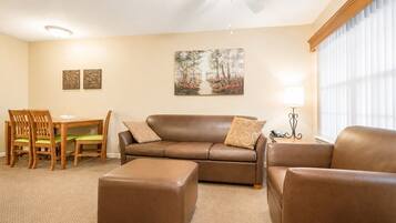 A living room with a brown leather sofa, matching ottoman, and a dining area with wooden chairs and a table.