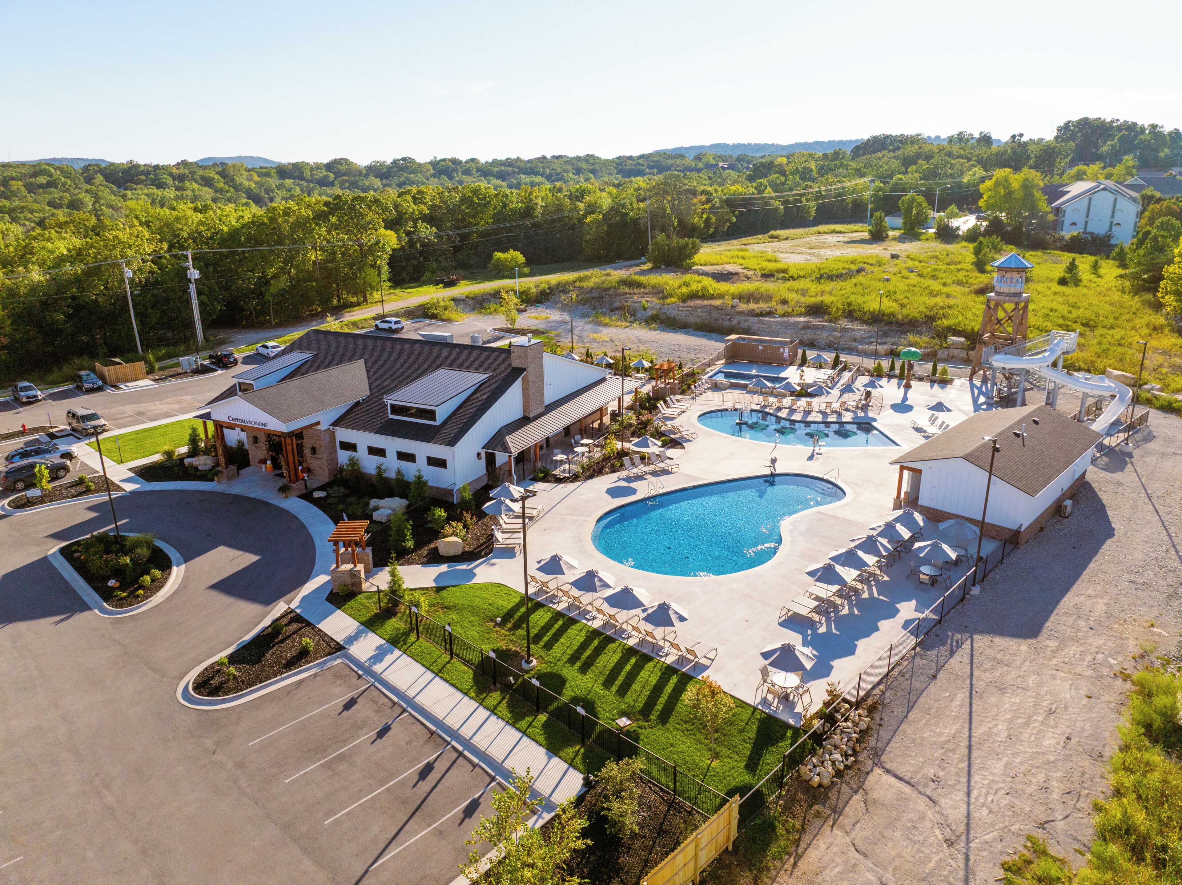 A resort with a swimming pool, lounge chairs, and a parking lot.