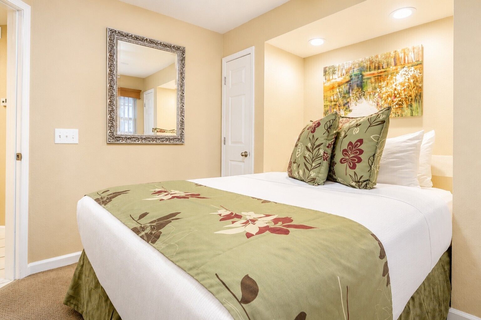 Una camera da letto con un letto, una coperta a fiori, uno specchio, una porta e un quadro appeso al muro.