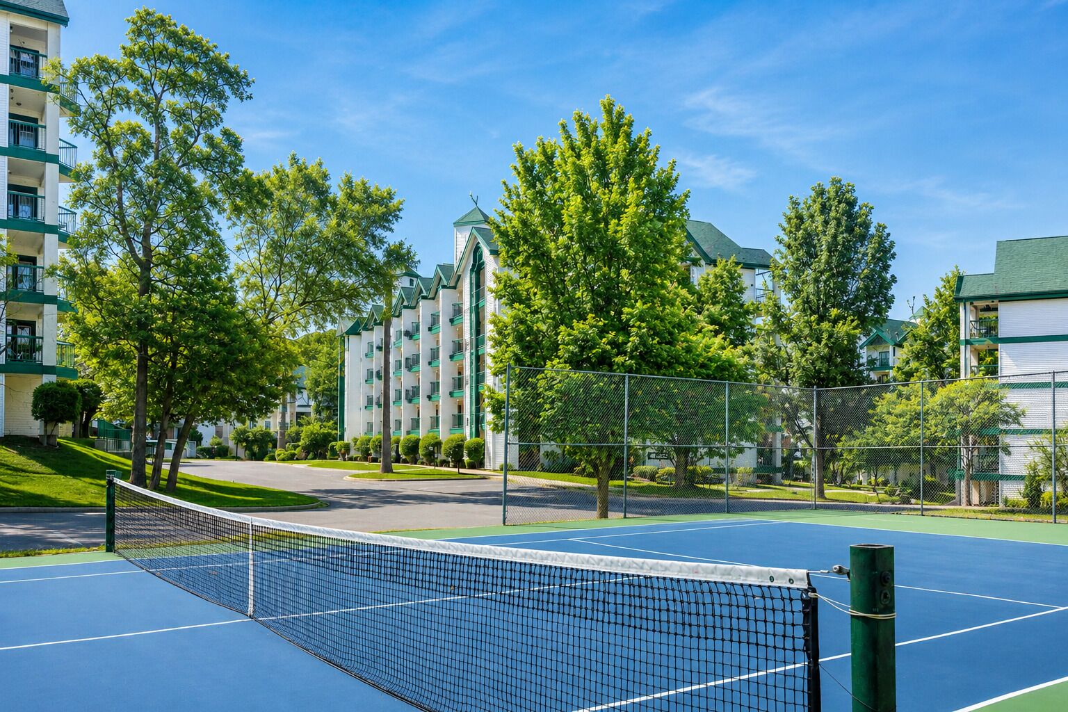 A tennis court with a net, surrounded by trees and a building with balconies.