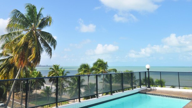 A poolside view with a clear sky, palm trees, and a beach in the background. - Nobile Inn Cabo Branco (João Pessoa)