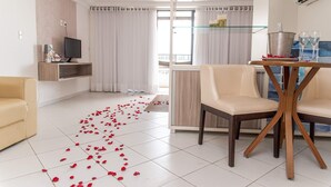 A modern living room with a television, a sofa, a dining table with chairs, and a balcony with curtains. - Nobile Inn Cabo Branco (João Pessoa)
