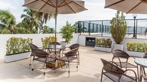 A rooftop patio with wicker furniture, umbrellas, and potted plants. - Nobile Inn Cabo Branco (João Pessoa)