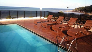 Una piscina al aire libre, sombrillas, sillones reclinables de piscina