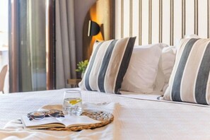 A neatly made bed with striped pillows, a glass of water with a lemon slice, and a pair of sunglasses on an open book. - Aretousa Hotel (Skiathos)