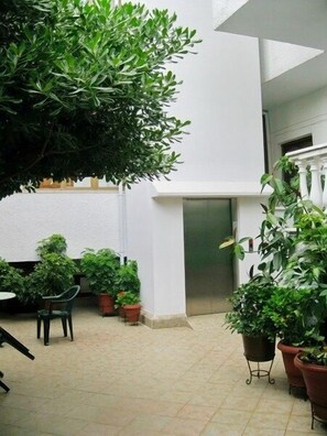 A courtyard with potted plants, a chair, and an elevator. - Aretousa Hotel (Skiathos)