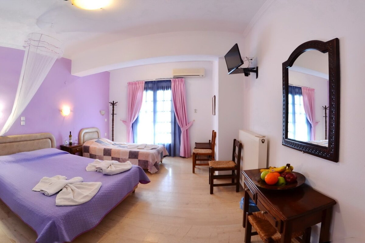 A bedroom with two beds, a desk with fruit, a mirror, and a chair.