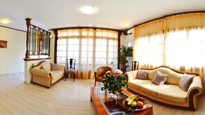 A living room with two sofas, a coffee table with fruit, a chair, and a bookshelf. - Aretousa Hotel (Skiathos)