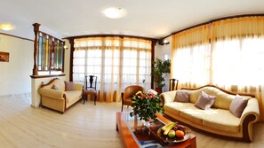 A living room with two sofas, a coffee table with fruit, a chair, and a bookshelf. - Aretousa Hotel (Skiathos)