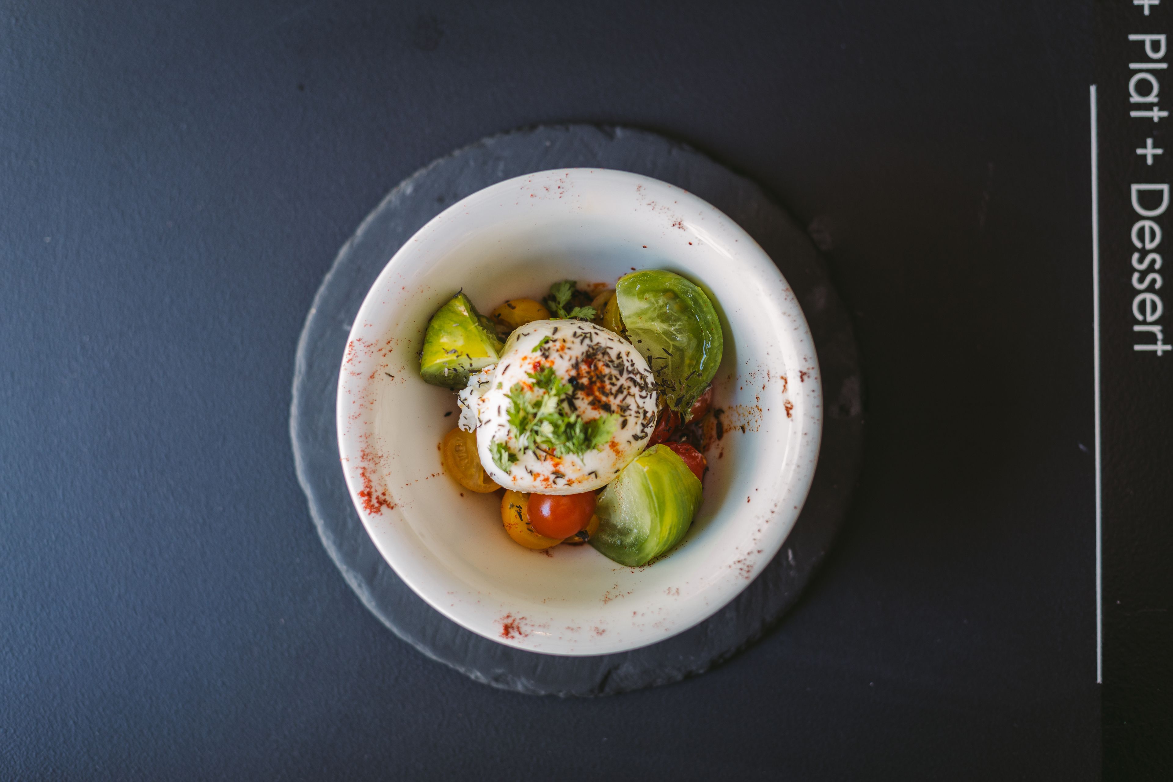 A white bowl with a salad on a dark surface.