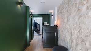 Un pasillo con paredes verdes, piso de madera, un armario negro y una pared de piedra.