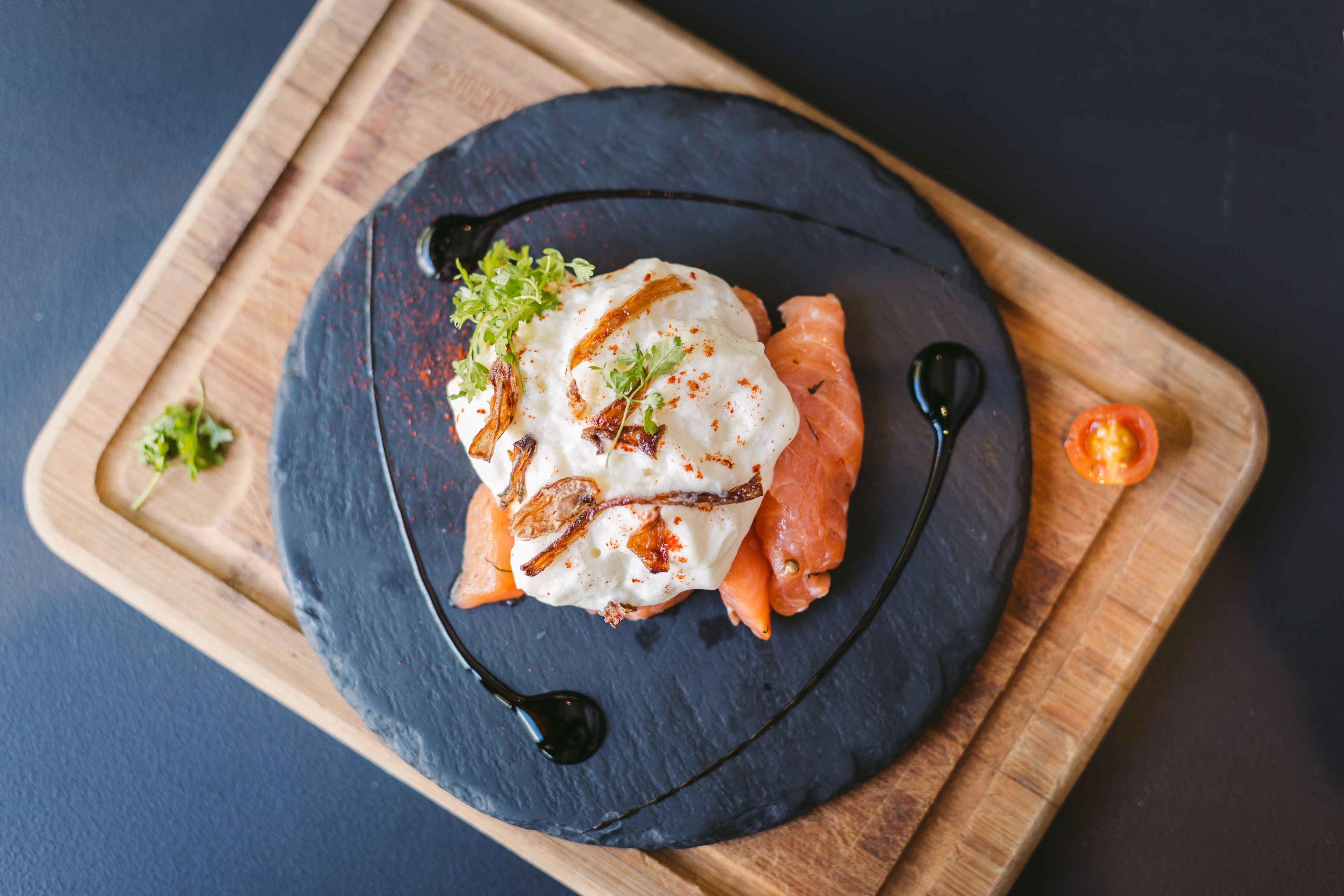 Un plat composé d’œufs pochés, de saumon fumé et de diverses garnitures, le tout présenté sur une assiette en ardoise.