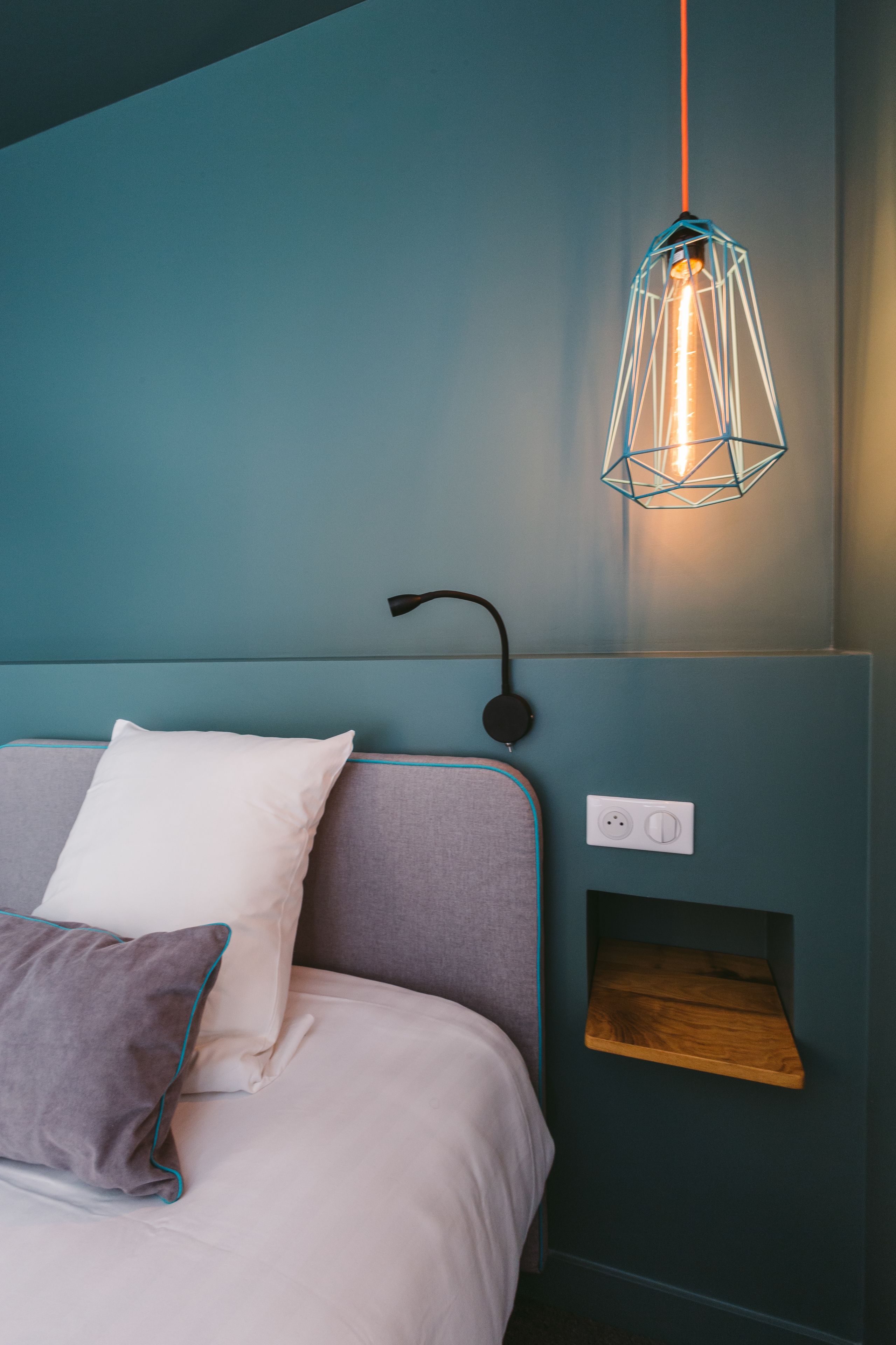 Una camera da letto con un letto, cuscini, una mensola a parete e un lampadario.