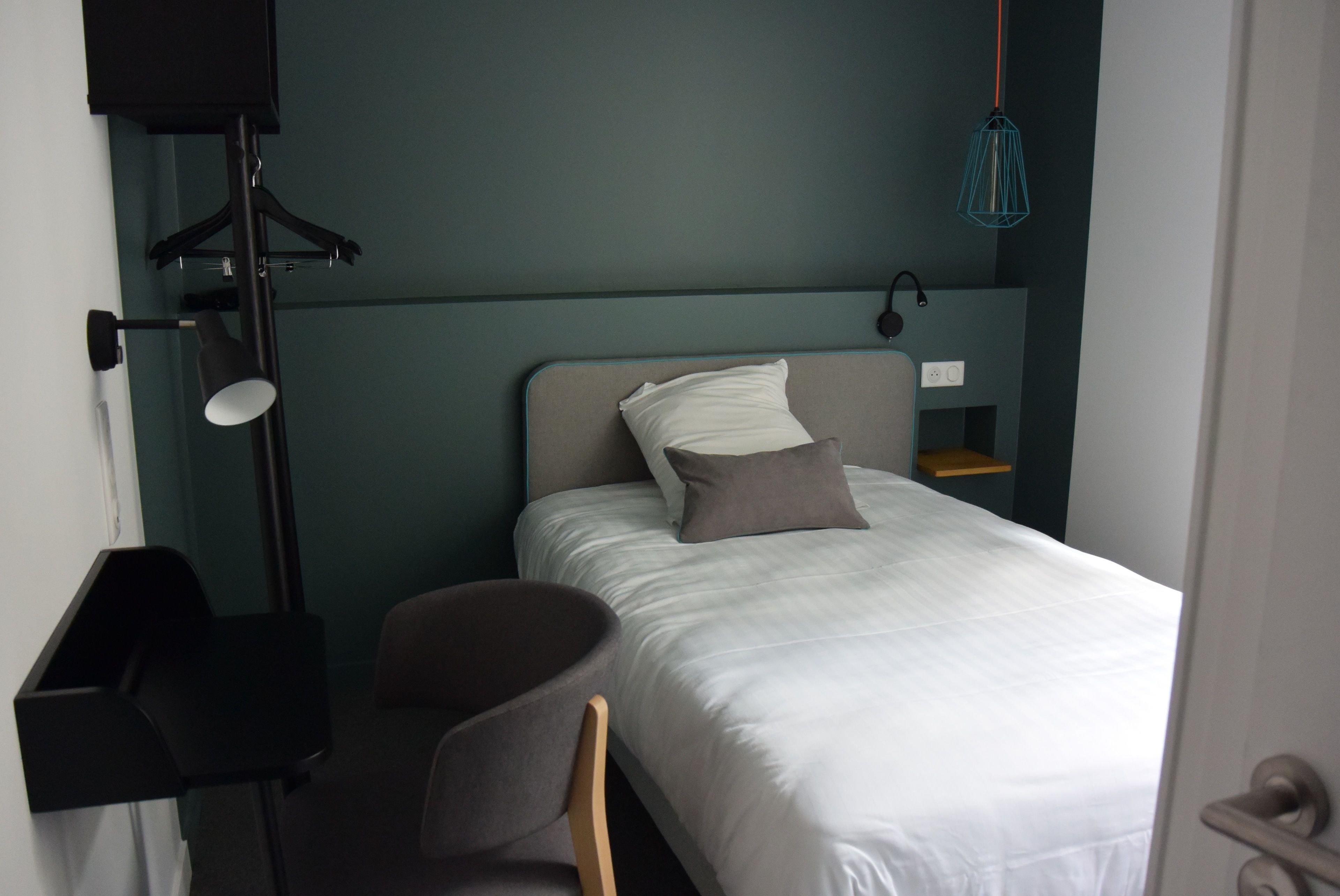 A bedroom with a bed, a chair, a desk, and a hanging light fixture.