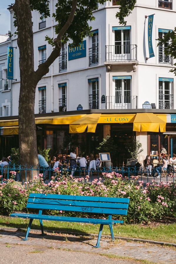 Un hotel con terraza y un banco azul al frente.