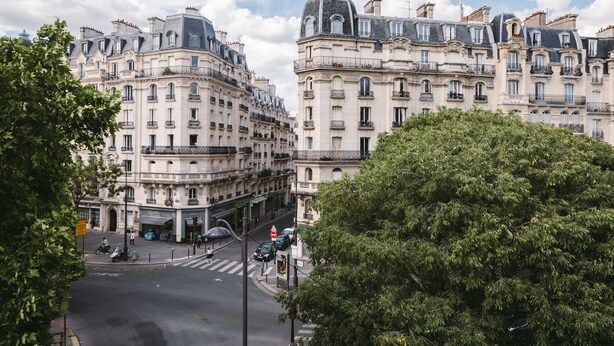 Vista de una calle con edificios de estilo europeo histórico, un paso de peatones y un árbol.