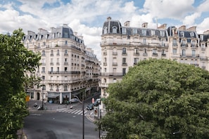 A street view with historic European-style buildings, a crosswalk, and a tree. - Le petit Cosy Hôtel (Paris)