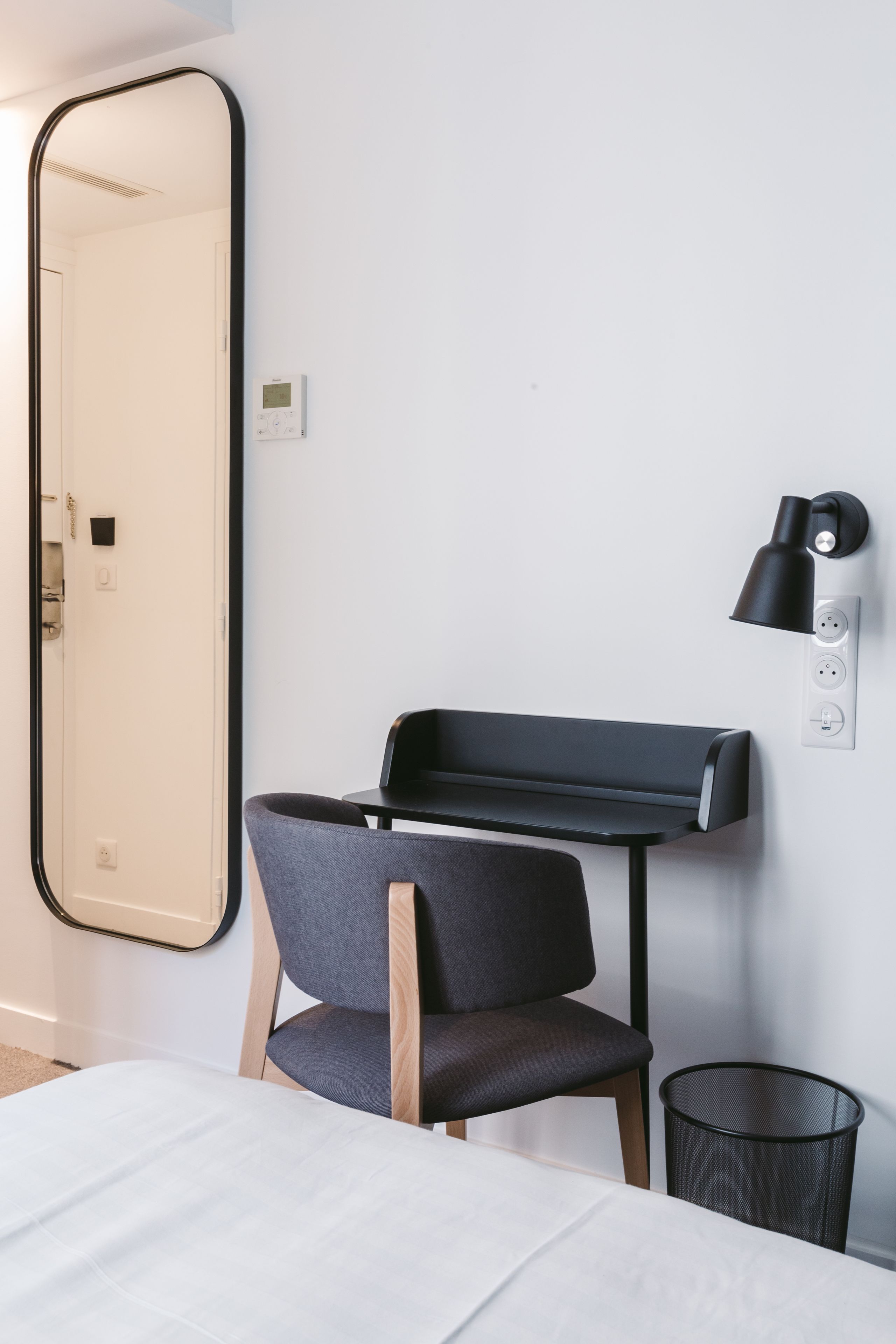 Una habitación de hotel moderna con un espejo grande, un escritorio con silla, una lámpara negra y un bote de basura.