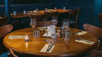Un restaurant avec des tables rondes en bois, chacune agrémentée de verres à vin, de verres à eau et de couverts.