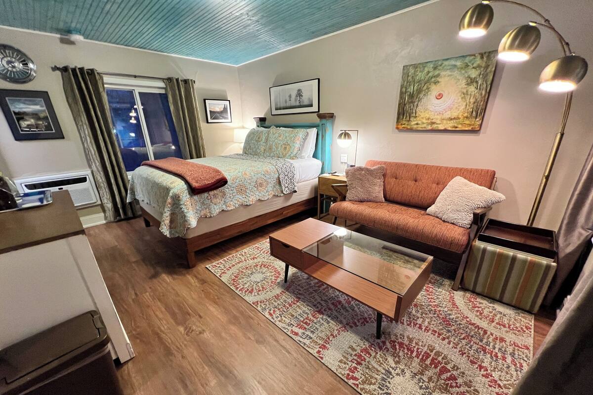 A hotel room with a bed, sofa, coffee table, and a painting on the wall.
