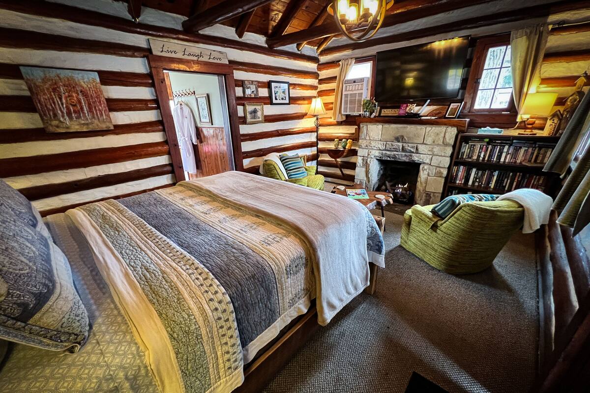 A cozy log cabin-style room with a large bed, a fireplace, a bookshelf, and a television.
