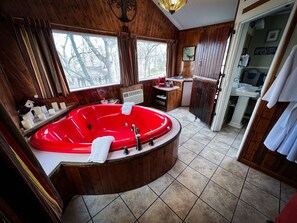 A wooden bathroom with a red bathtub, a sink, and a window.