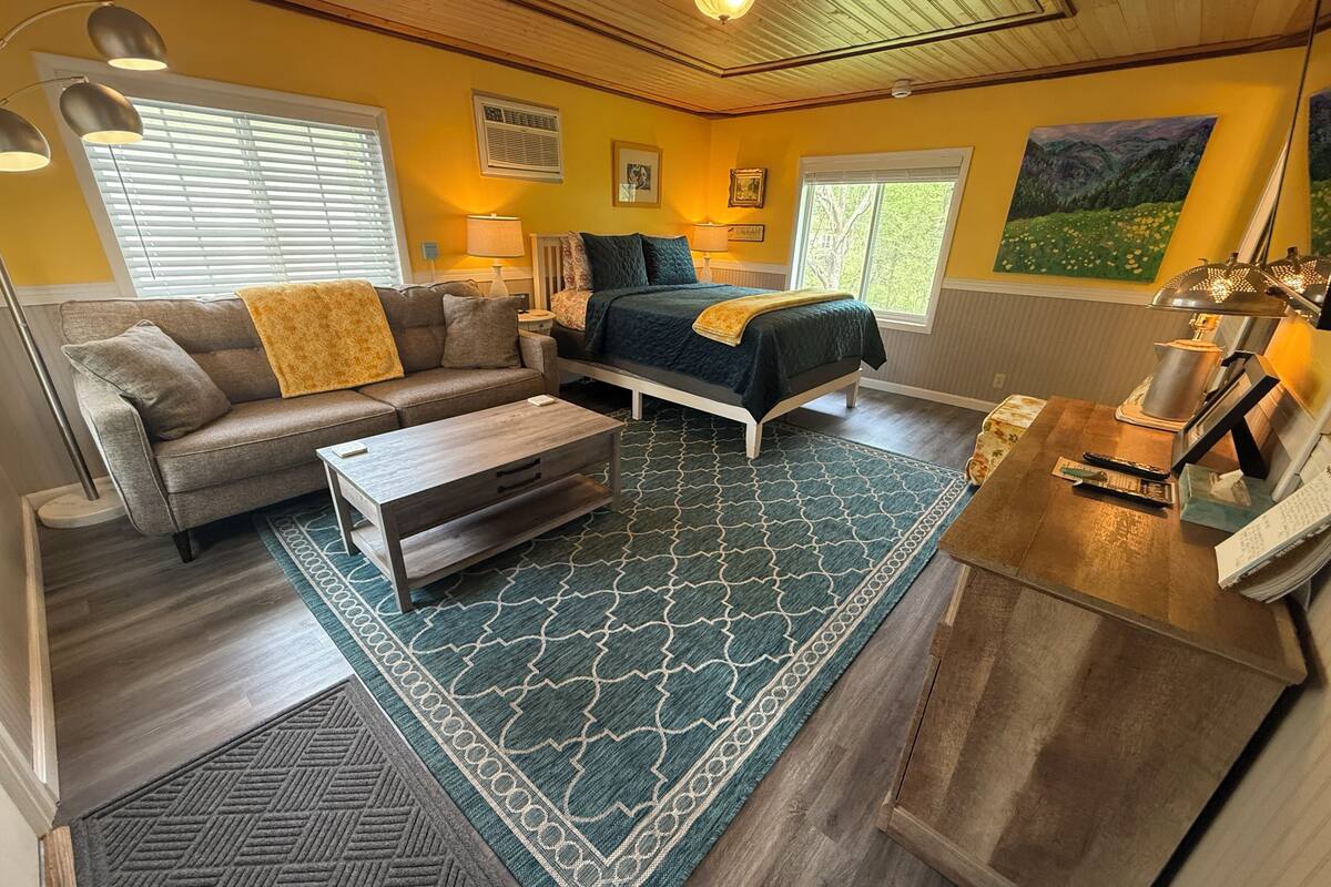 A compact living space with a sofa, a bed, a coffee table, and a desk with a lamp.