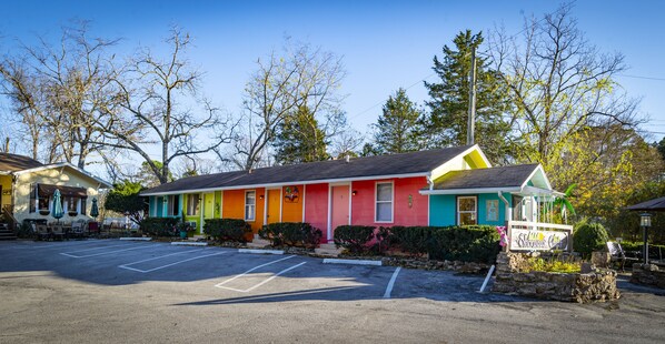 A colorful motel with a parking lot and trees in the background.
