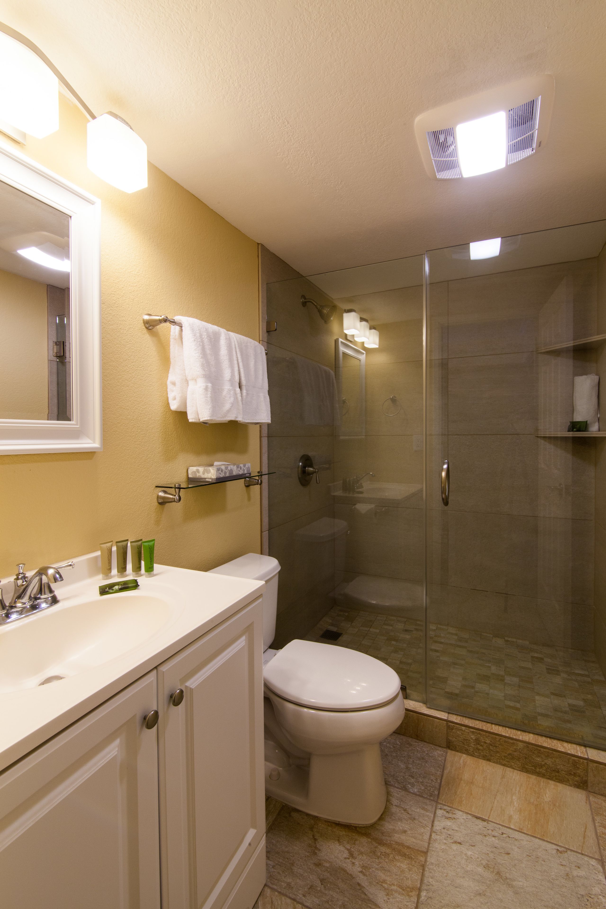 A bathroom with a white sink, mirror, and toilet, a glass shower enclosure, and beige walls.