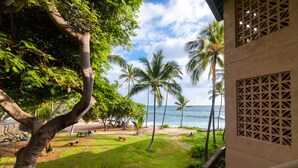 A view of a beach with palm trees and a building with a lattice window design. - Kona Reef, A Raintree Vacation Club Resort (Kailua-Kona)