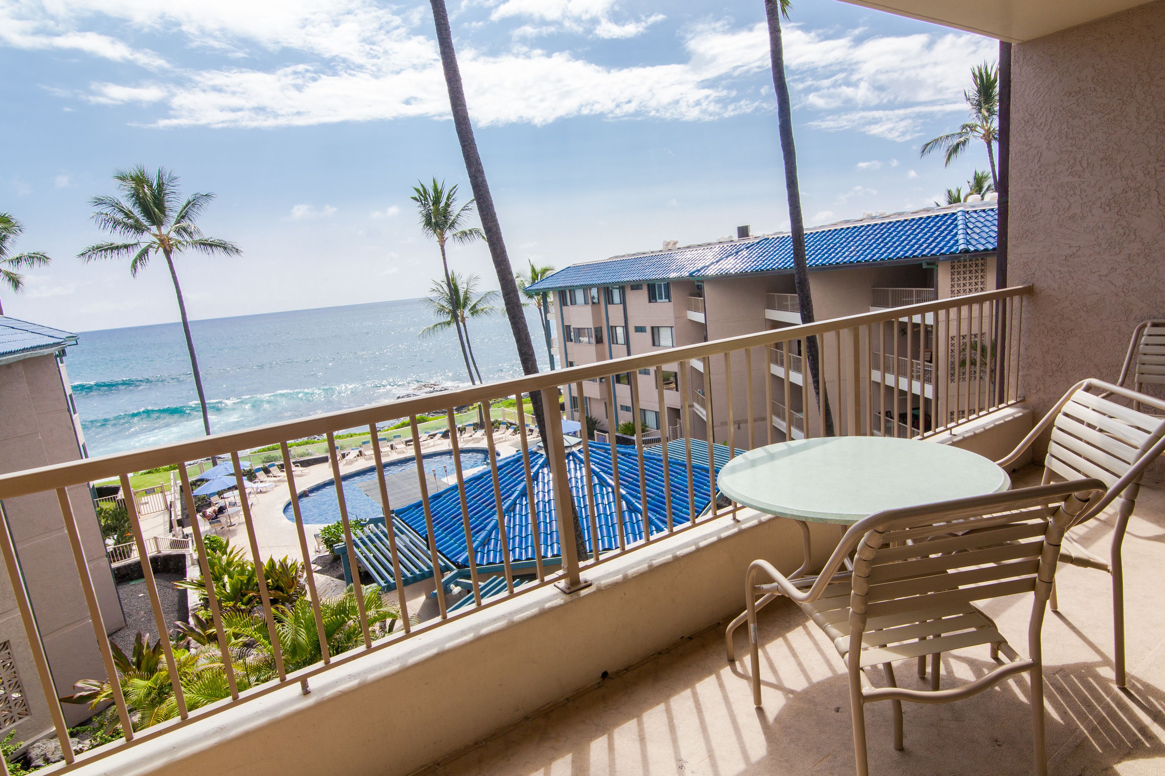 A balcony with a view of a swimming pool, palm trees, and the ocean.