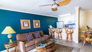 A living room with a brown sofa, a glass coffee table, wicker chairs, and a ceiling fan. - Kona Reef, A Raintree Vacation Club Resort (Kailua-Kona)