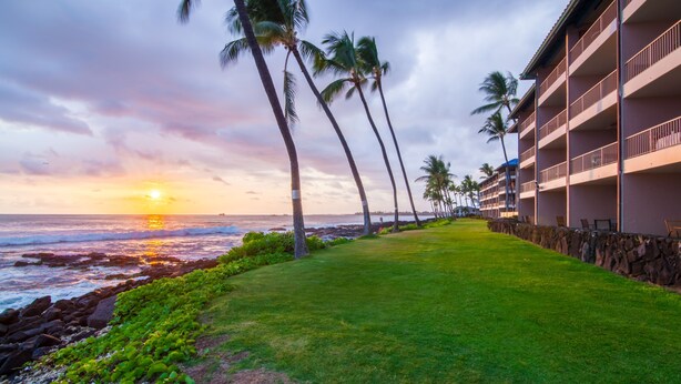A beachfront hotel with a grassy pathway lined with palm trees, overlooking the ocean at sunset. - Kona Reef, A Raintree Vacation Club Resort (Kailua-Kona)