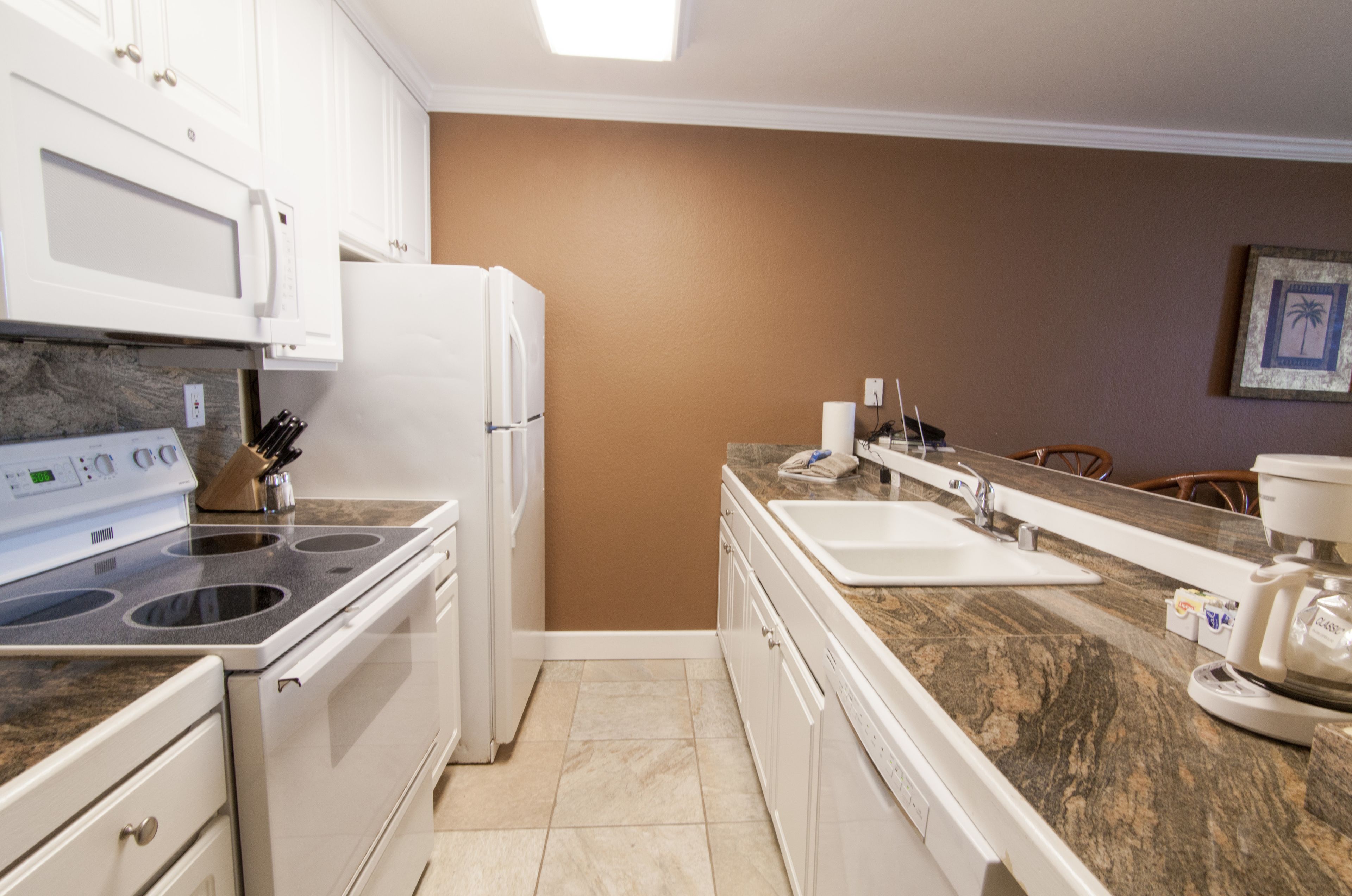 Una cocina compacta con electrodomésticos blancos, encimera de granito y pared marrón.