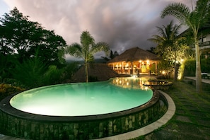 A swimming pool with a stone edge, surrounded by tropical vegetation and palm trees. - Teras Bali Rice Terrace Bungalows and Spa (Sidemen)