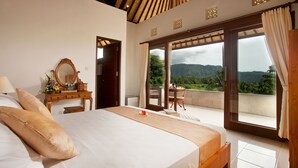 A bedroom with a large bed, a wooden dresser, a mirror, and a balcony with a view of the mountains.