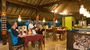 A restaurant with wooden tables and chairs, a thatched roof, and a counter with a mural.