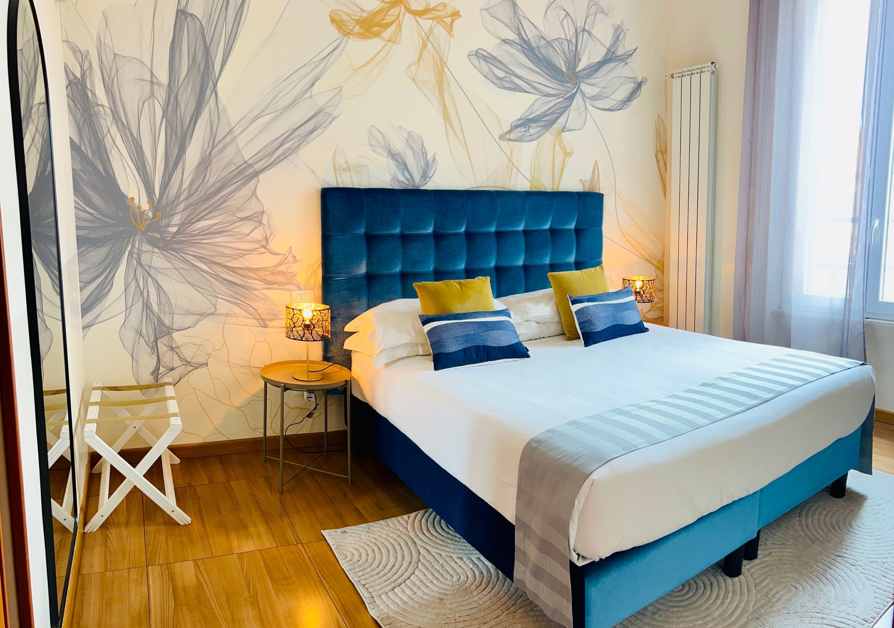 A bedroom with a large bed, a nightstand, a chair, and a wall with floral patterns.