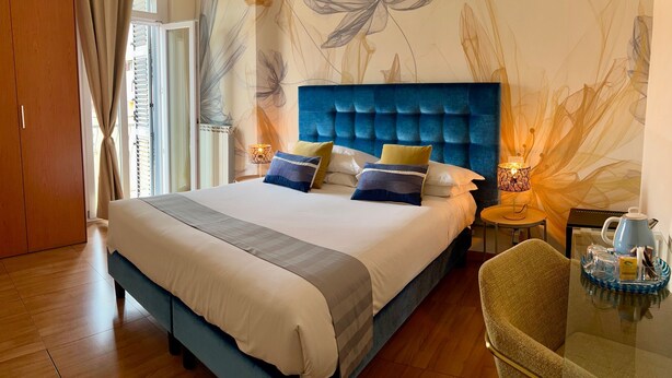 A bedroom with a large bed, a blue headboard, and a floral wall mural. - Bon Ton Design Rooms by DOT Suites (Rome)