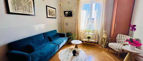 A modern living room with a blue sofa, a round coffee table, patterned chairs, and a large window with curtains.