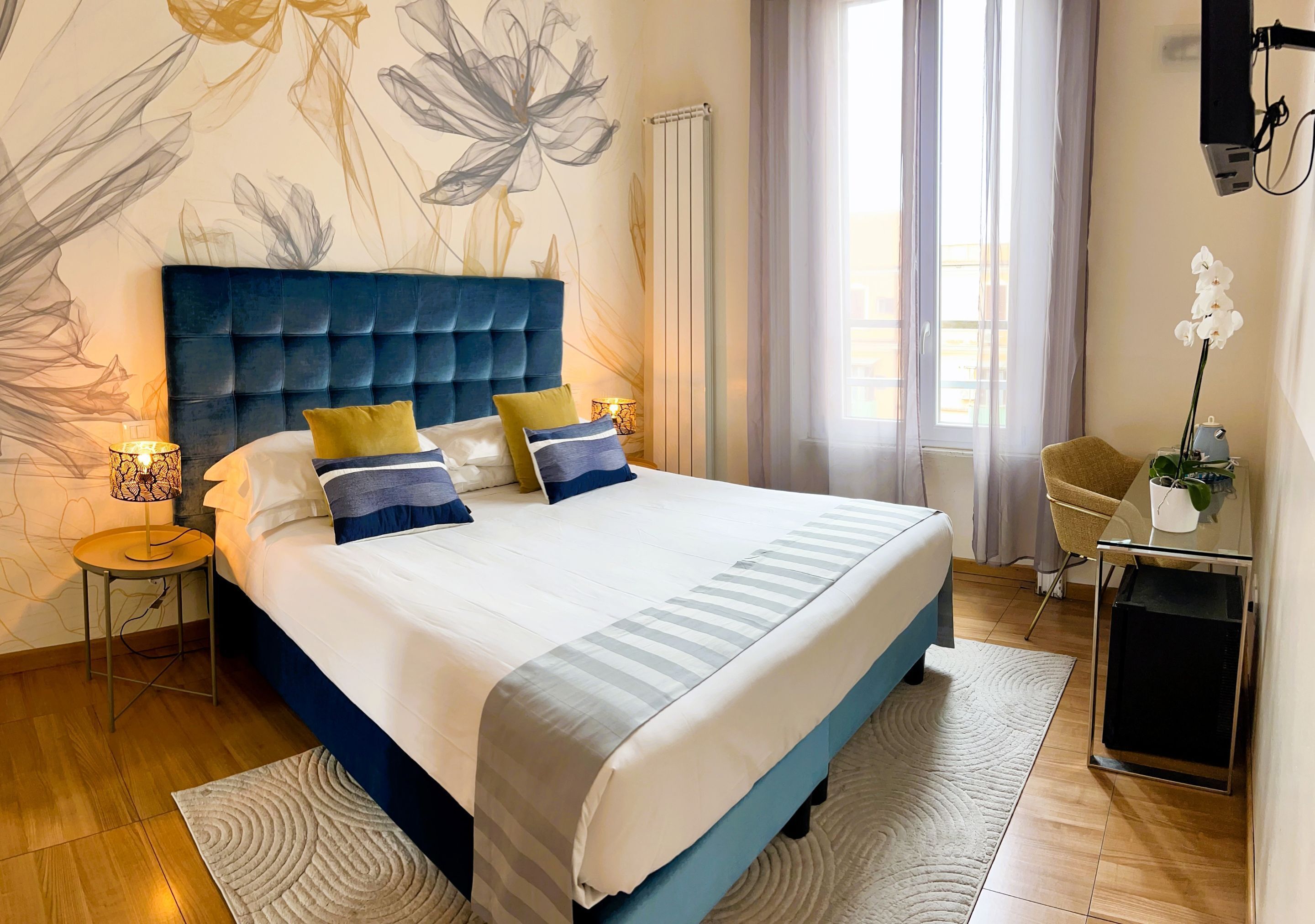 A neatly arranged bedroom with a large bed, a bedside table with a lamp, a chair, and a small table with a plant.