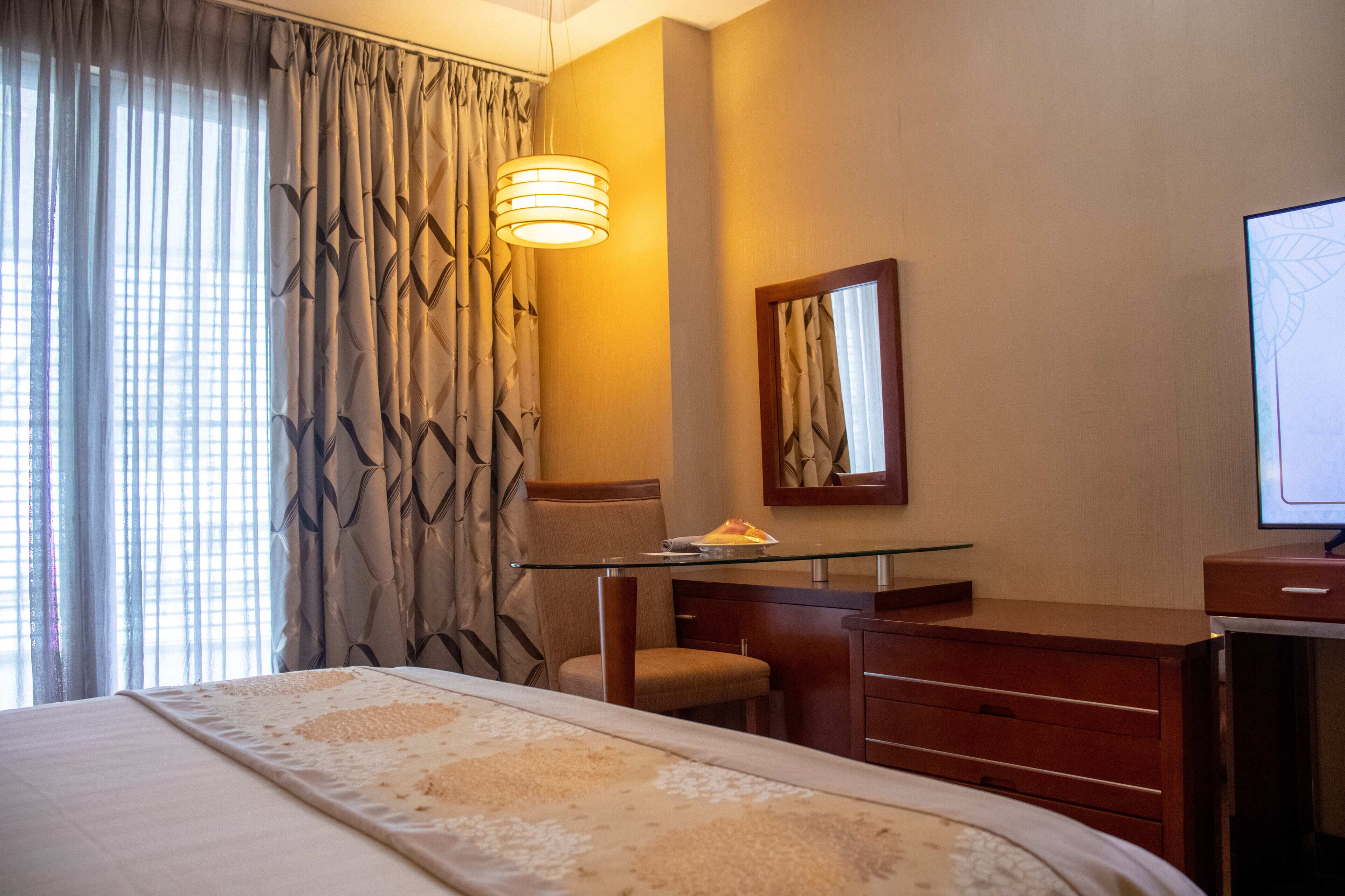 A hotel room with a bed, a desk with a chair, a television, and a window with curtains.