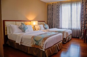 A hotel room with two beds, a nightstand, a lamp, and a window with curtains.