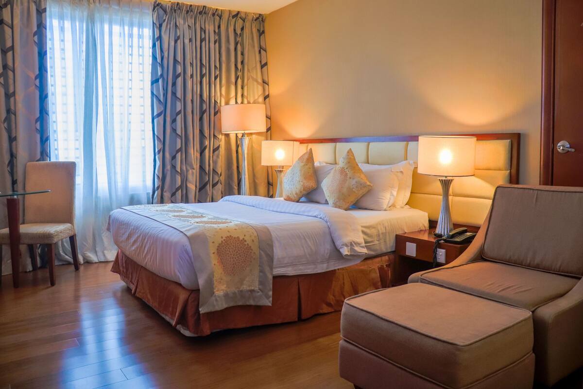 Ein Hotelzimmer mit einem großen Bett, zwei Nachttischlampen, einem Sessel und einem Schreibtisch.