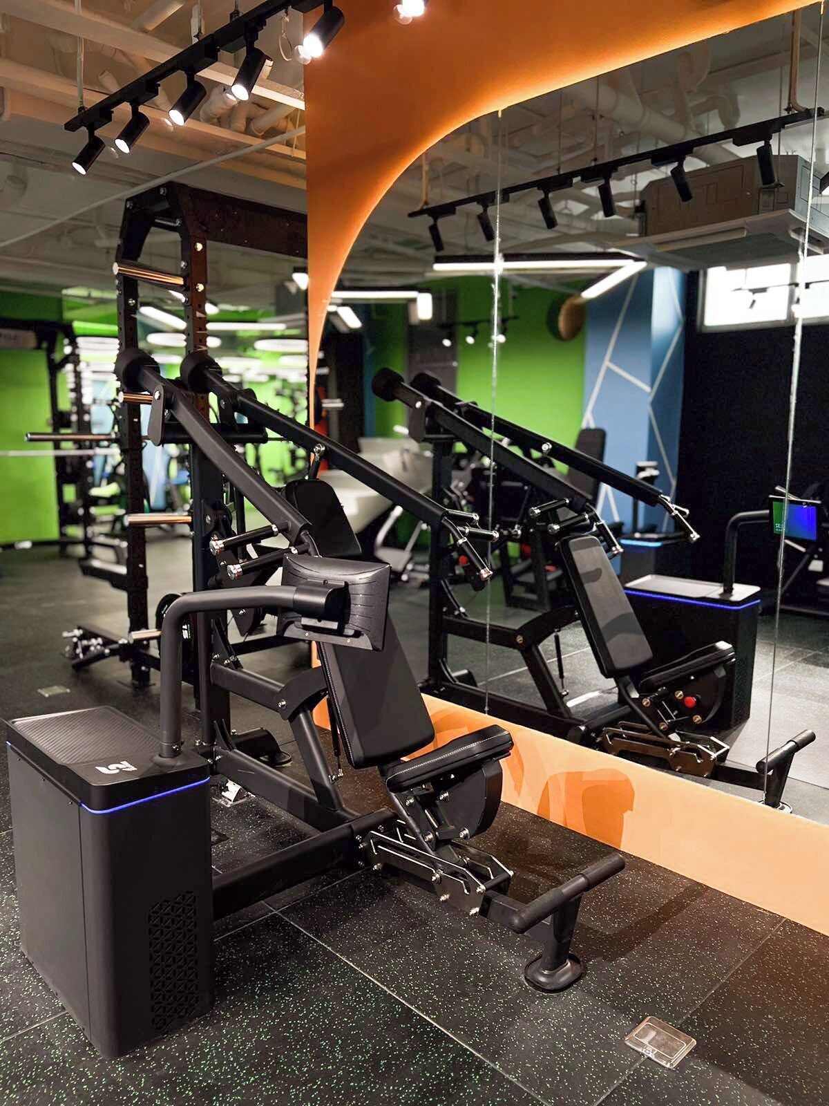 A gym with weightlifting equipment, a mirrored wall, and green and blue walls.