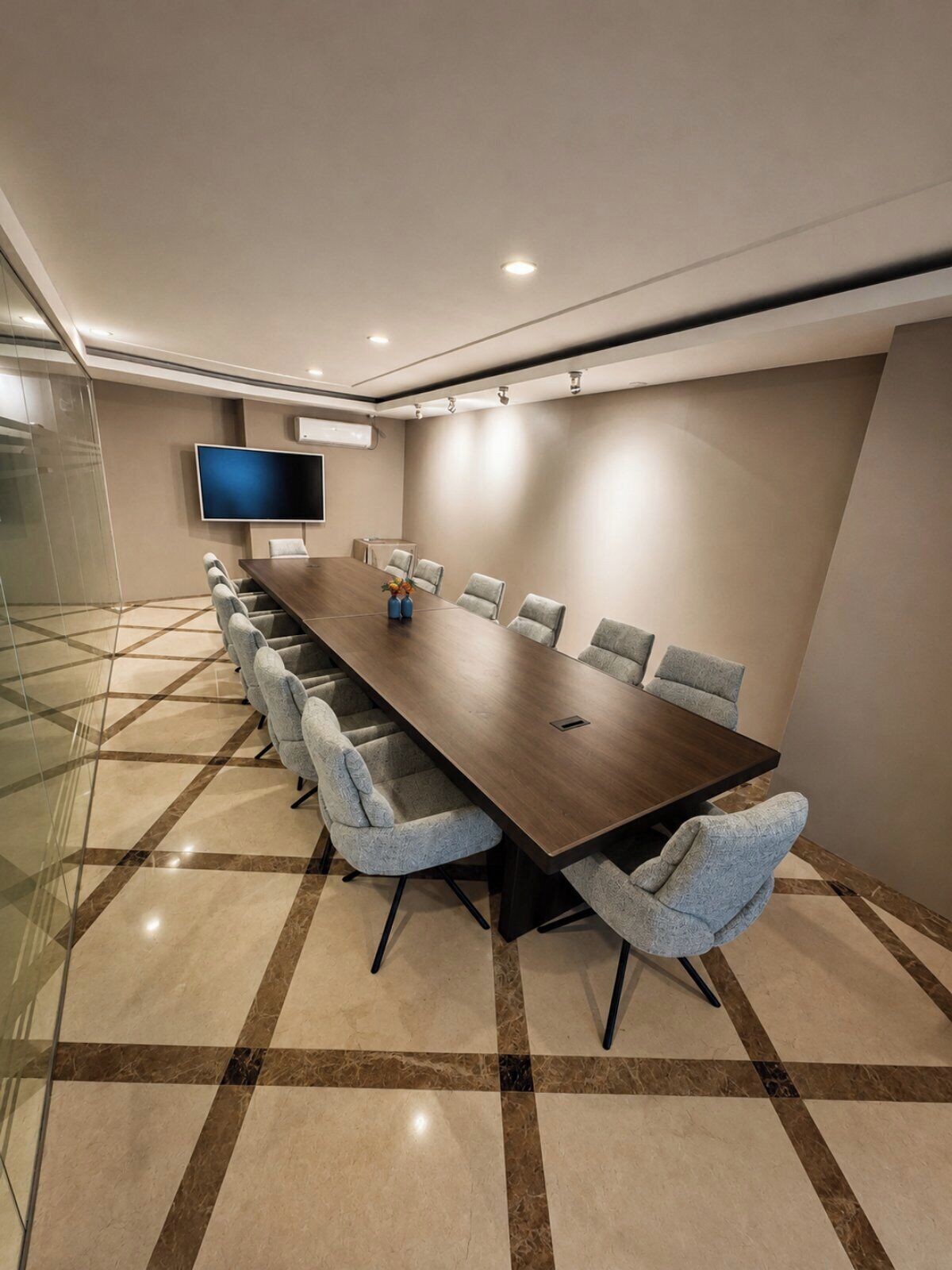 A conference room with a long table, several chairs, a flat-screen TV, and a tiled floor.