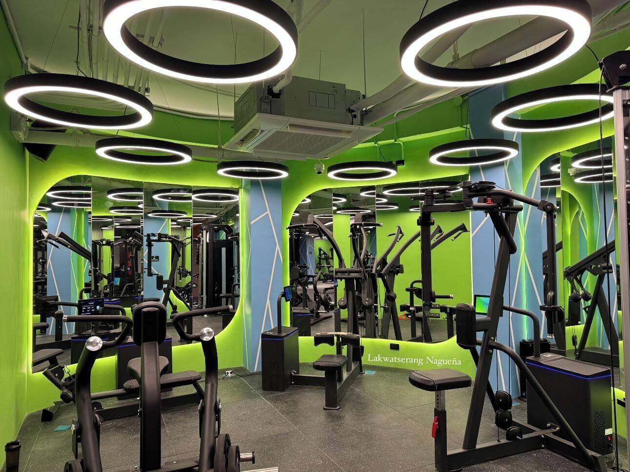 Een sportschool met trainingsapparatuur, spiegels en groene wanden.